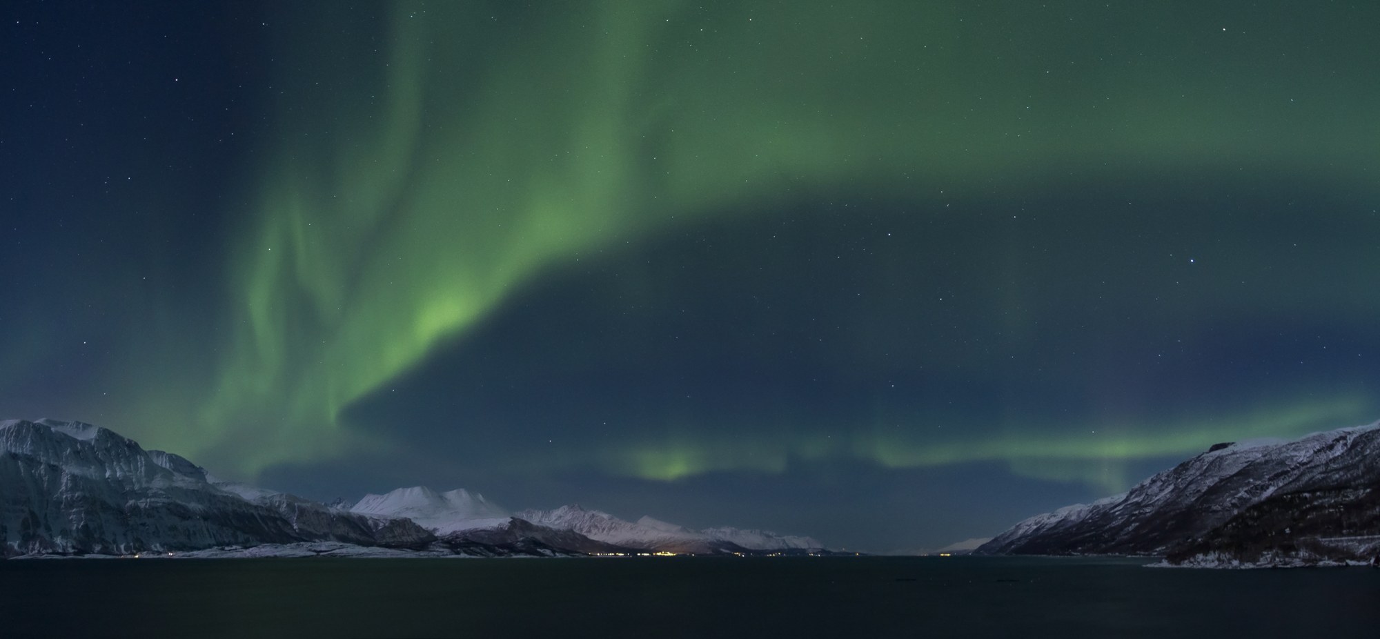 Aurora boreal verde sobre el fiordo de Lyngen y montañas nevadas en Noruega